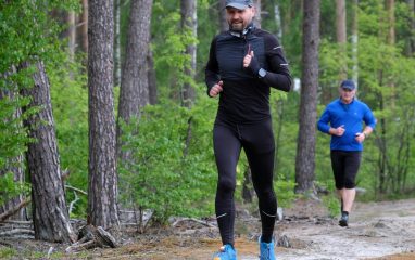 Outdoor exercise scene with two men jogging through a lush green forest trail, wearing sports attire.
